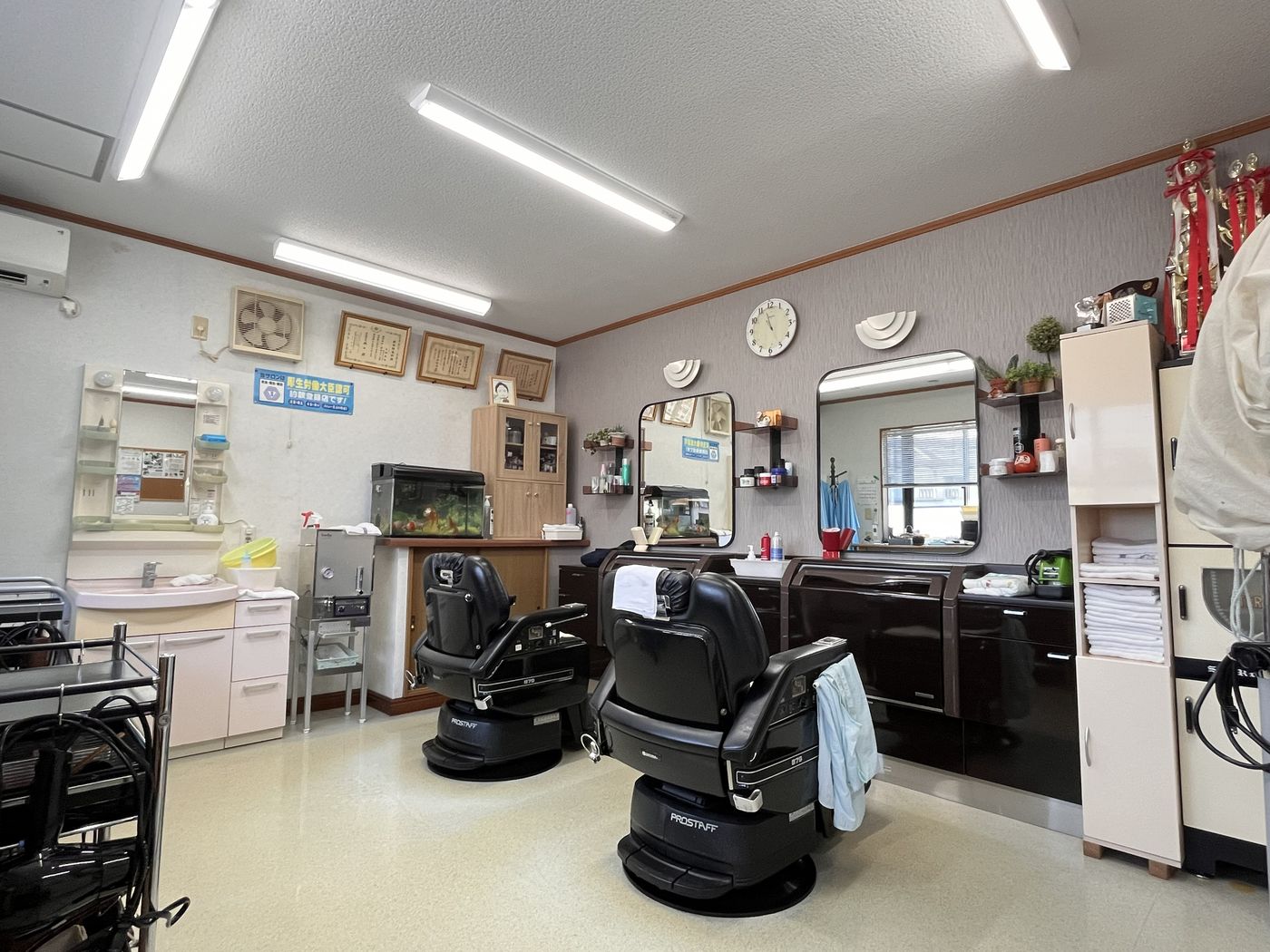 カットハウス トバの店内。2台の理容椅子と鏡、壁には表彰トロフィーが並ぶ