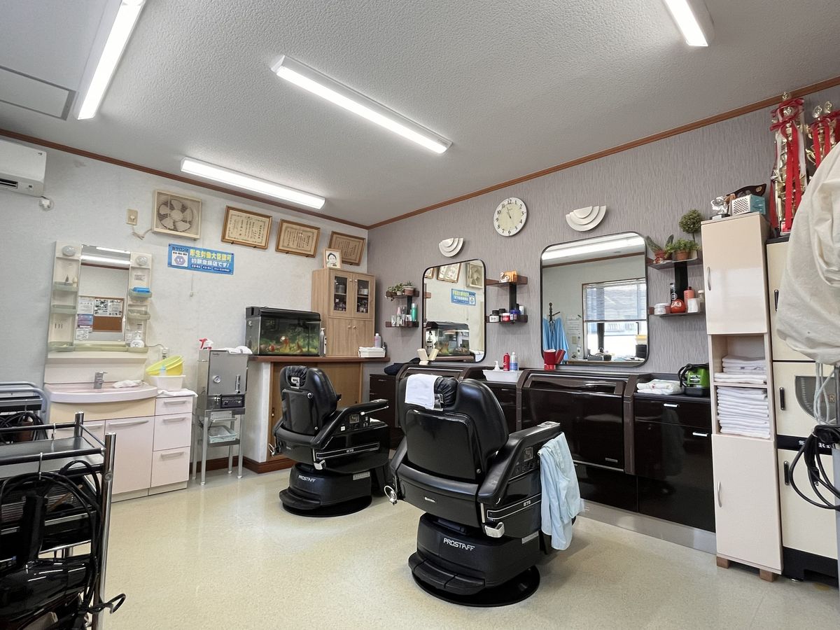 明るい店内。2台の理容椅子と大きな鏡、右手の棚には受賞トロフィーが並ぶ