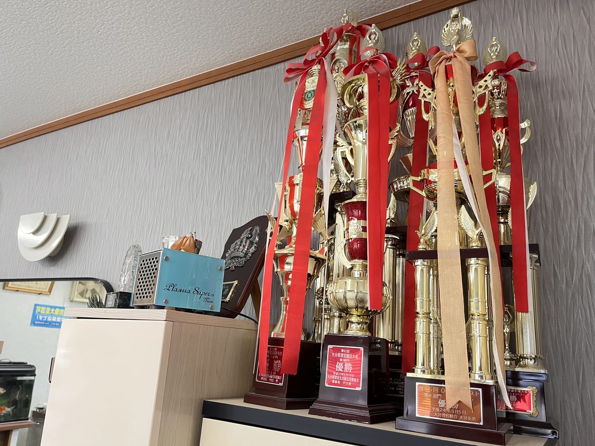 店内に飾られた優勝トロフィー。赤いリボンを付けた大分県理容競技大会のトロフィーが幾重にも並ぶ