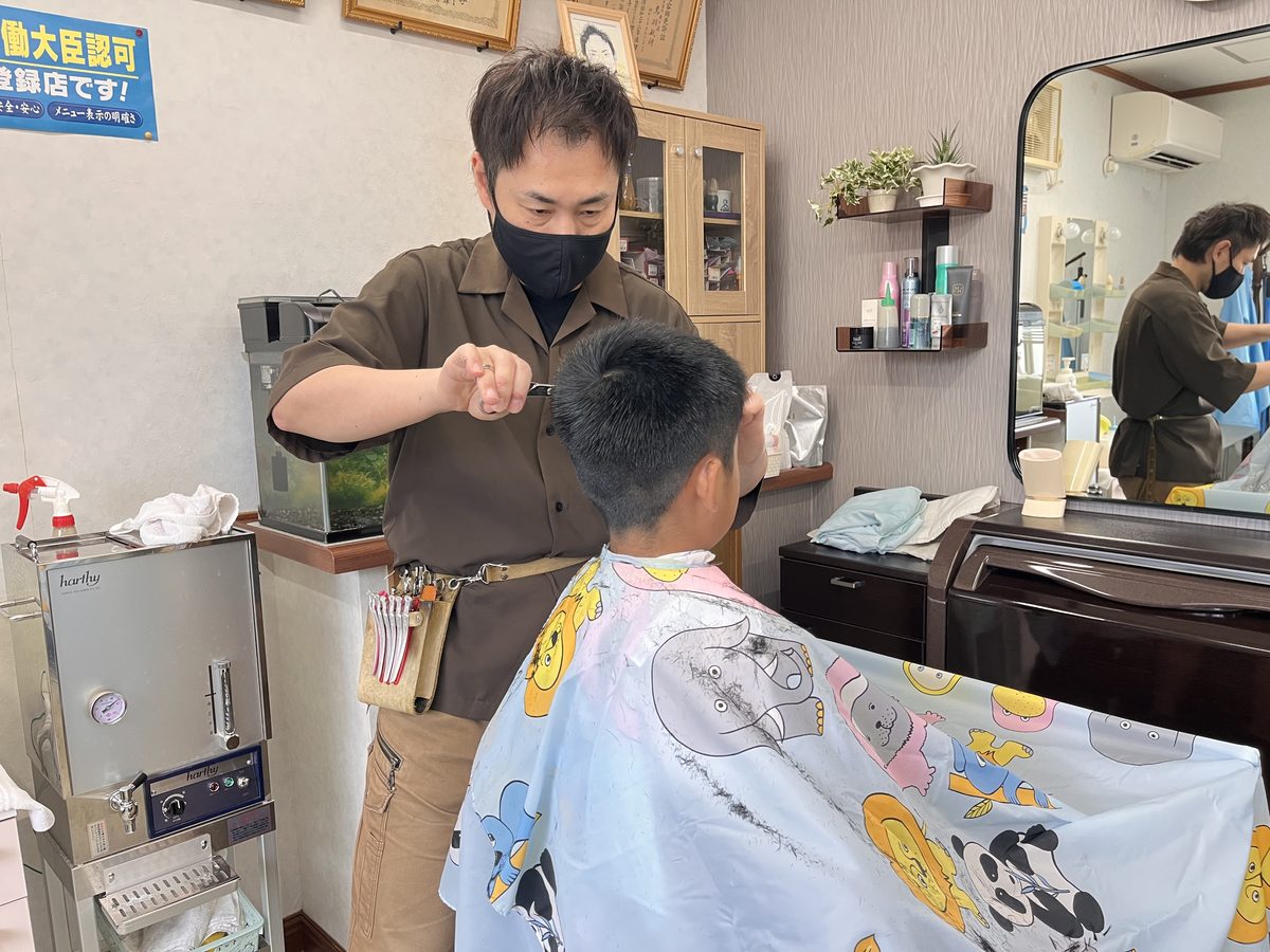 理容師がお子様の髪をはさみで整えているようす。明るい店内で施術を受ける子ども