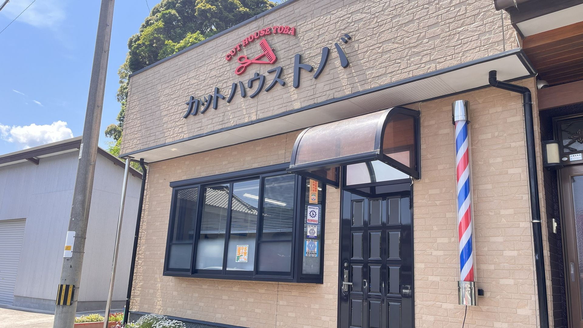 カットハウス トバの外観。青空の下、看板とサインポールが見える店舗正面